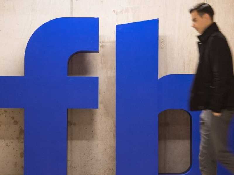 Un uomo cammina davanti al logo di Facebook al quartier generale di Londra in Rathbone Place (foto LaPresse)