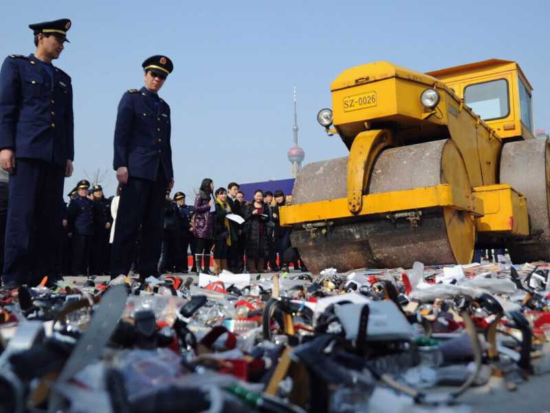 Poliziotti guardano un rullo compressore che schiaccia prodotti contraffatti a Shanghai (Foto di Getty Images)&nbsp;<br />