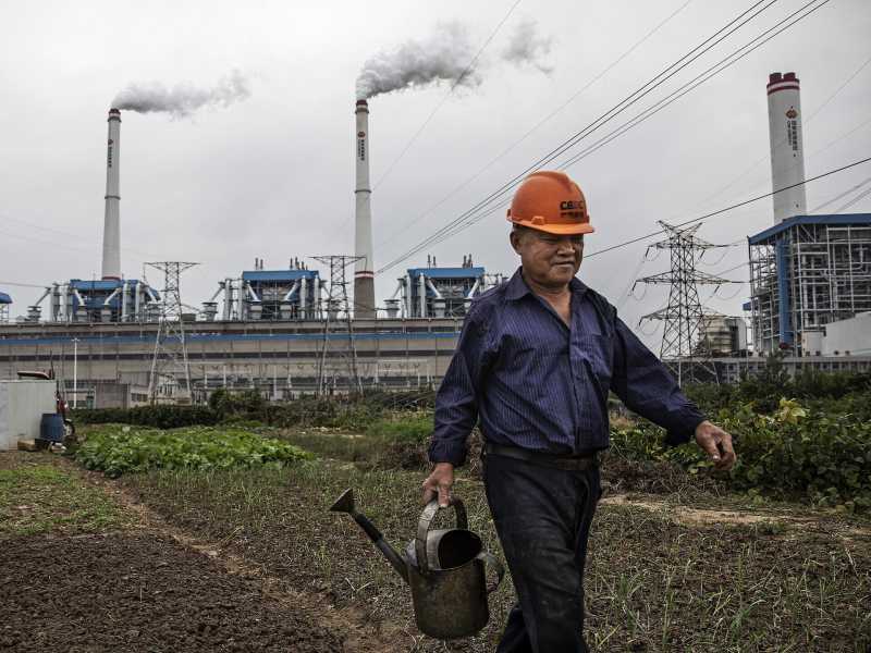 Un uomo annaffiare l'orto di fronte a una centrale elettrica a carbone il 13 ottobre 2021 a Hanchuan, provincia di Hubei, Cina (Getty Images) <br />