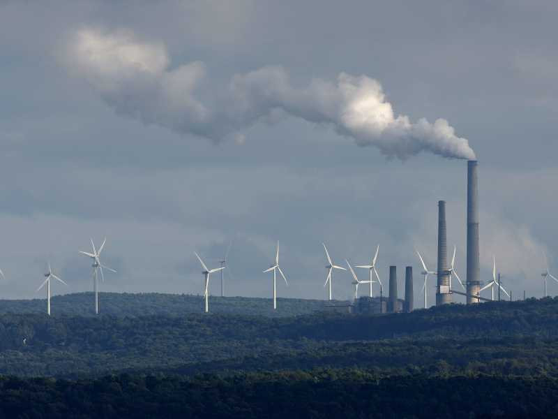 &nbsp;Delle pale eoliche vicino a una ciminiera (Getty Images)