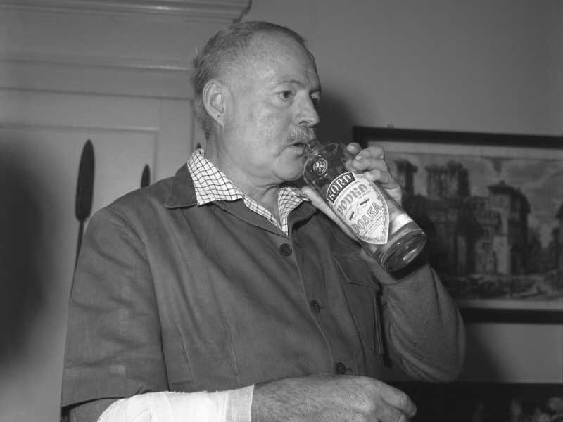 Ernest Hemingway, con il braccio ferito bendato, mentre beve vodka dalla bottiglia, Venezia 1954 (Getty Images)<br />