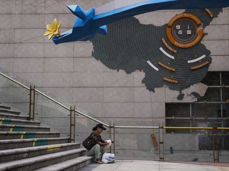 Una donna sistema la spesa vicino a una mappa che mostra i progetti di sviluppo di Evergrande, Pechino, 18 settembre 2023 (AP Photo/Andy Wong) 