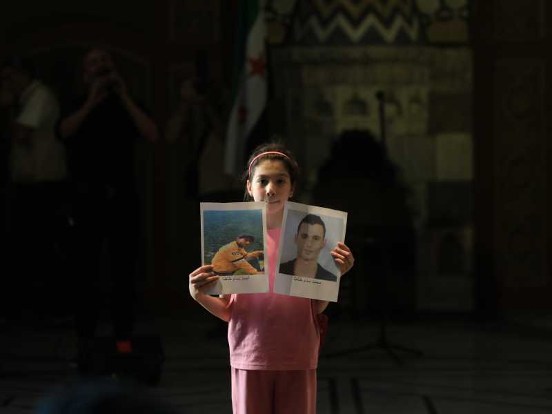 &nbsp;Una bambina mostra le foto di un parente scomparso all'evento del Museo nazionale di Damasco (foto Getty)