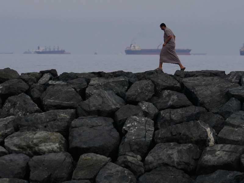 Un uomo cammina lungo la riva mentre petroliere e navi cargo sono in fila nello Stretto di Hormuz, visto da Khor Fakkan, Emirati Arabi Uniti, 11 marzo 2026. (Foto Ap/Altaf Qadri)
