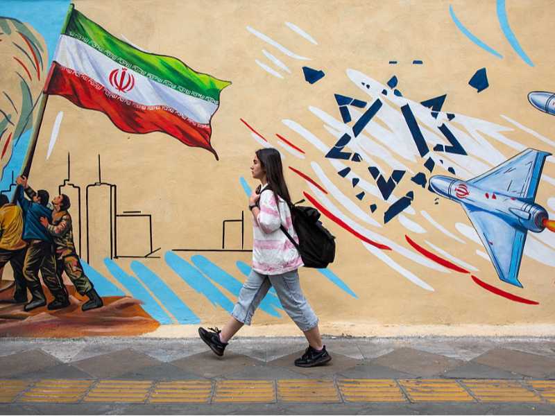Una donna passa davanti a un murale filogovernativo a Teheran (Photo by Majid Saeedi/Getty Images)