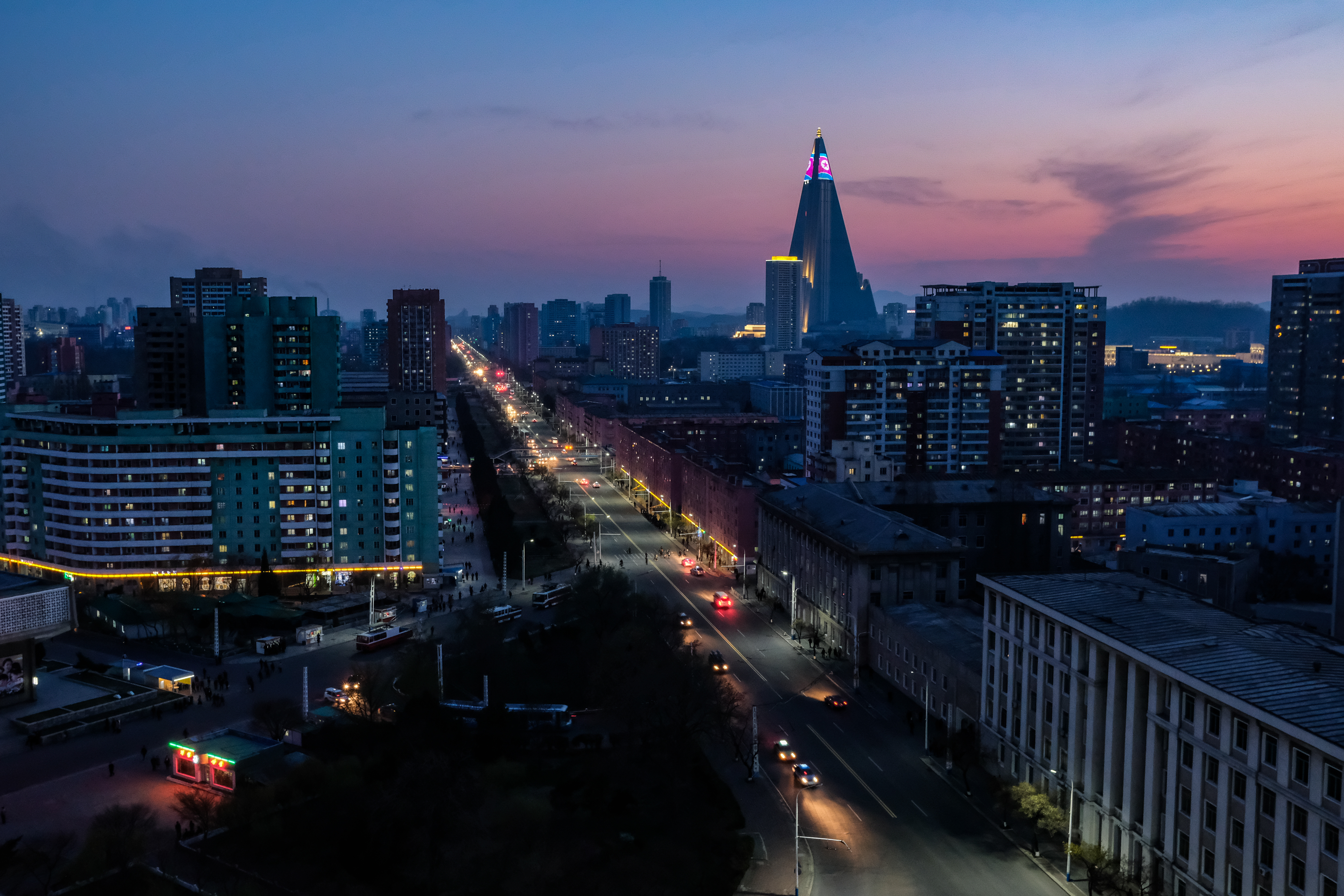 Pyongyang, 16 aprile 2018. La bandiera della Corea del nord viene proiettata sulla facciata dell’Hotel Ryugyong al tramonto. Dall’Arco di Trionfo, nel cuore della capitale, si osservano i larghi viali ancora attraversati da poche automobili prima che la notte avvolga la città